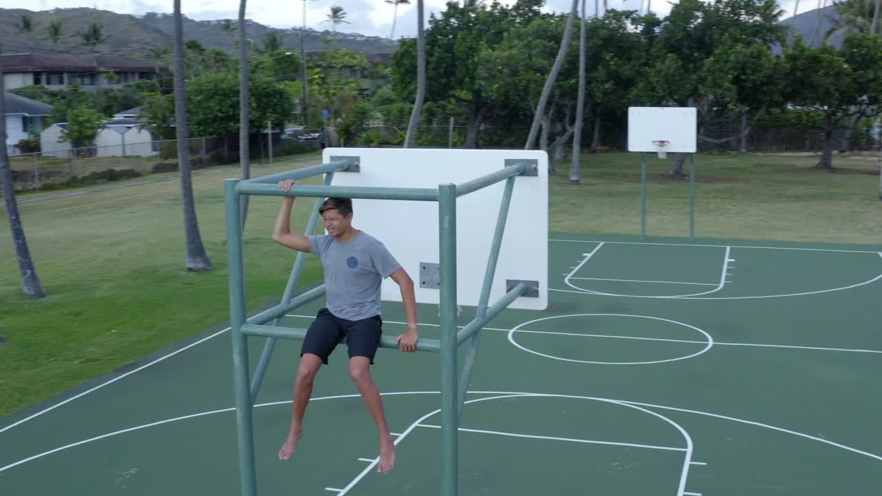 niño se sienta en el tablero de baloncesto en la cancha rodeado de palmeras