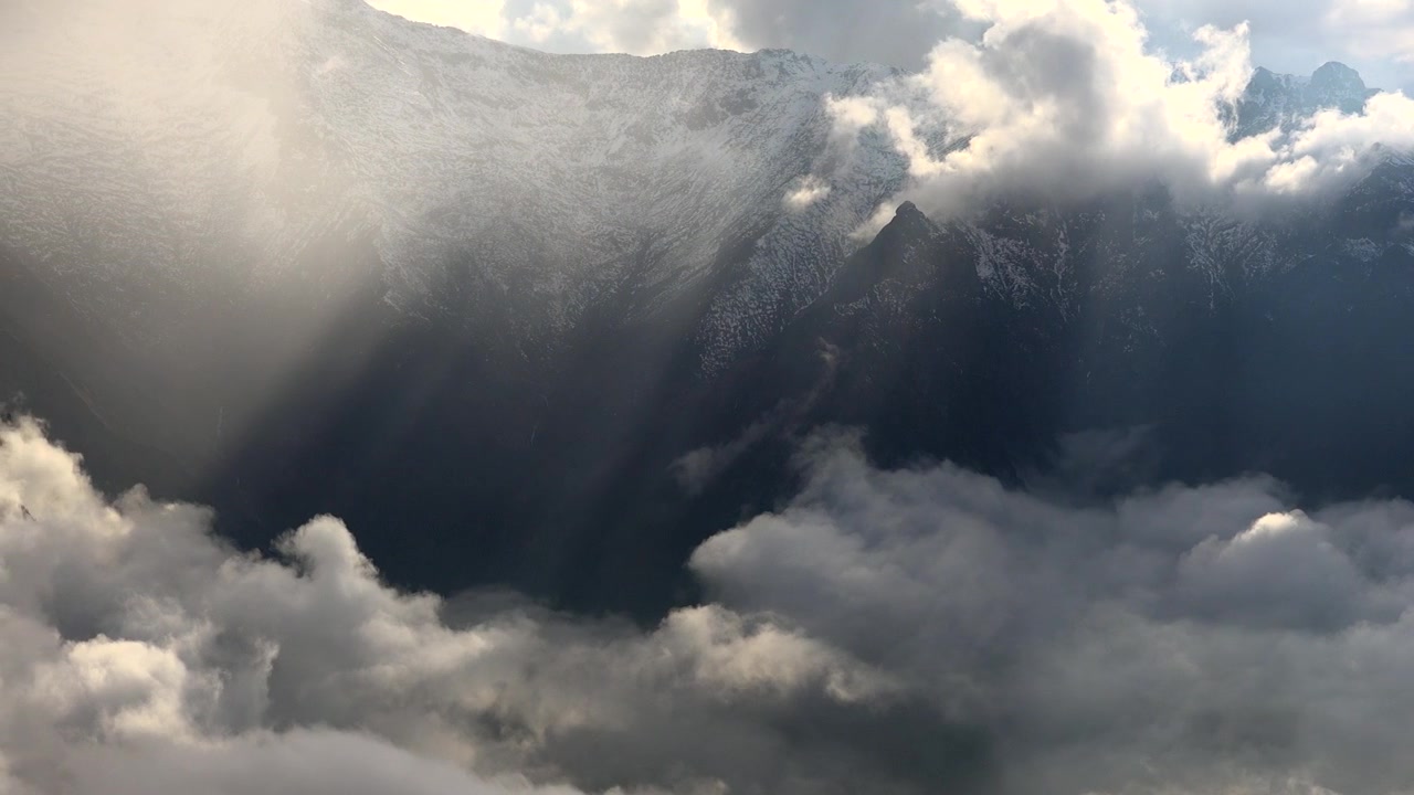 Sunlight Streaming Over Snow-Capped Mountain Peaks Above Clouds