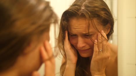 una mujer con moretones y cicatrices en la cara por haber sido golpeada y golpeada se mira en el espejo del baño y se limpia las lágrimas de la cara
