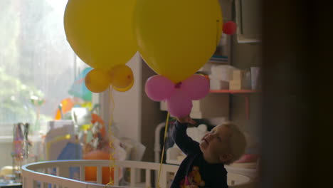 a baby girl standing in a crib and playing with balloons