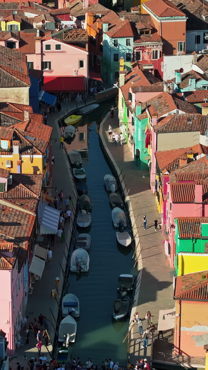 Aerial drone view of boats on the sides of a canal near the colourful houses of Burano. Vertical