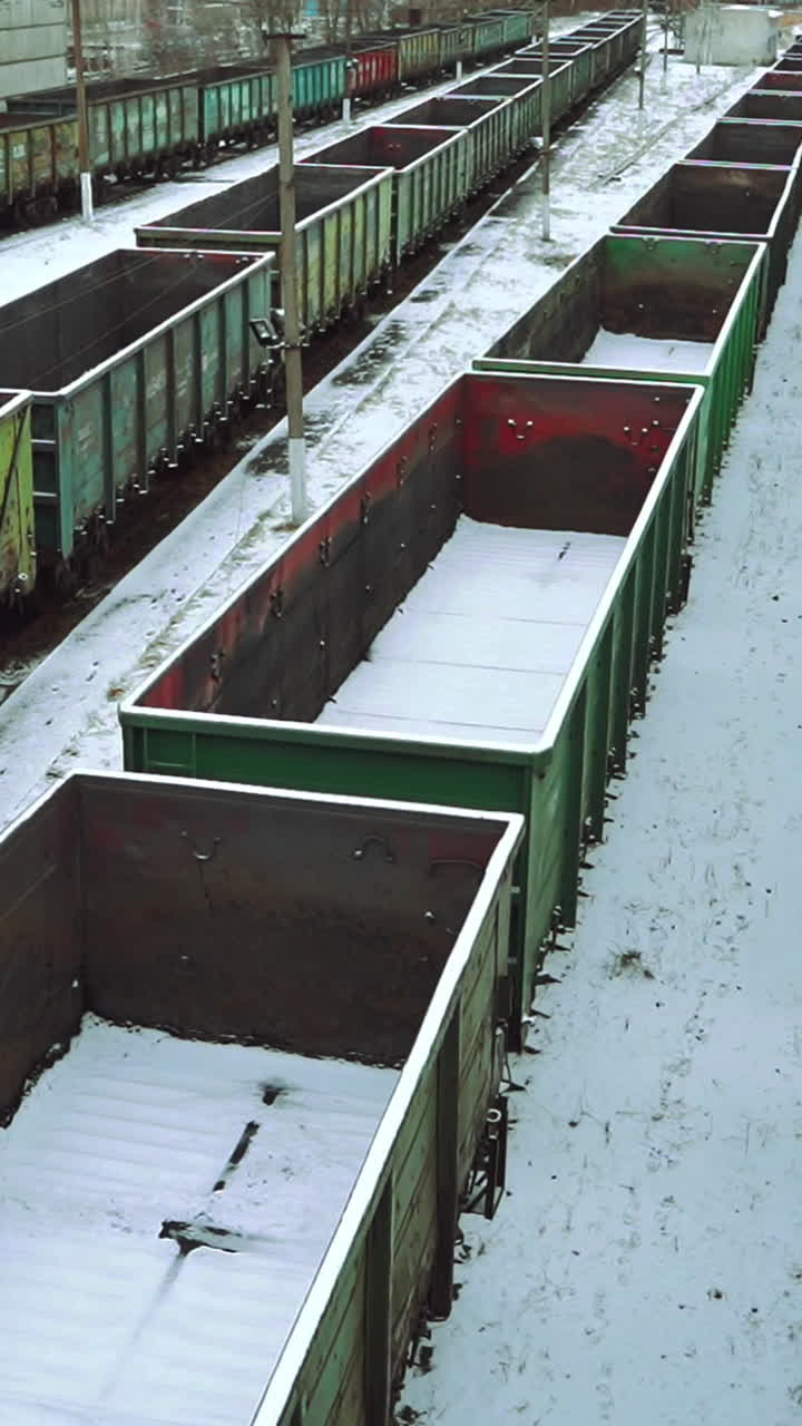 View of the rows with empty containers for the supply of goods, sprinkled with snow on the background of the railway station outside the city. Logistics. Vertical video