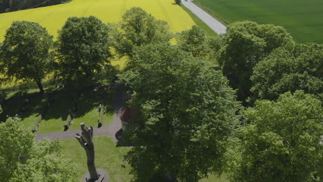 Vista-De-Drones-Sobre-Una-Pequeña-Casa-Rodeada-De-árboles-Y-Un-Gran-Campo-De-Canola-Amarillo