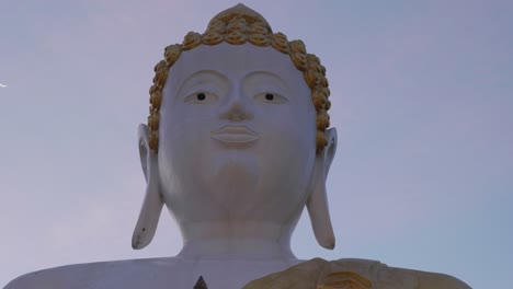 4k cinematic religious travel footage of a giant statue of buddha at the temple of wat phrathat doi kham in chiang mai, northern thailand during a beautiful sunset on top of a mountain