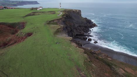 Stunning-Shot-Over-Sheep-Grazing-In-Green-Meadow-Near-Ajo-Lighthouse,-Cantabria,-Spain