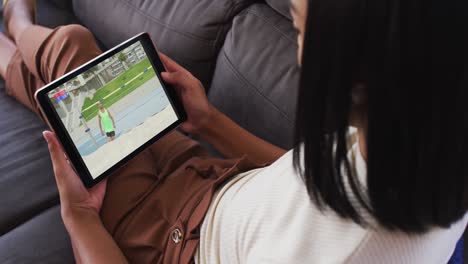 Compuesto-De-Mujer-En-El-Sofá-En-Casa-Viendo-Un-Evento-De-Salto-De-Altura-De-Atletismo-En-Una-Tableta