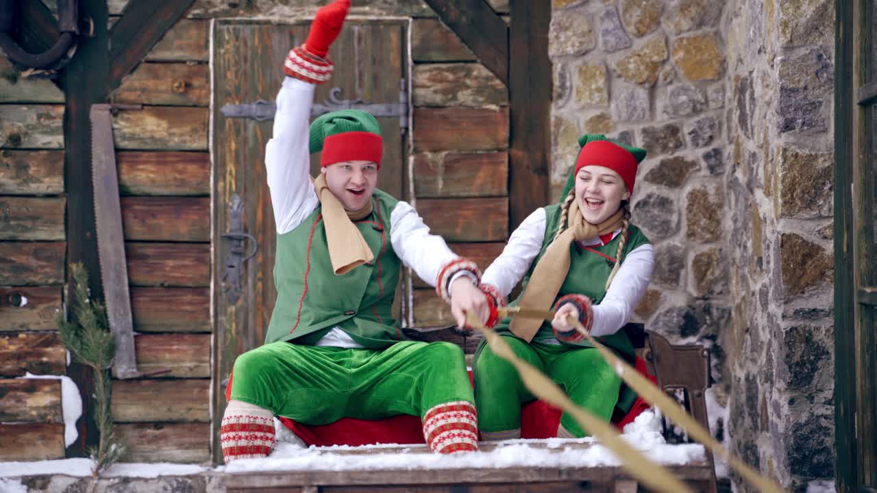 Christmas elves ride wooden sledges. New Year is coming. Christmas eve. Boy and girl wear christmas clothes. Having fun.