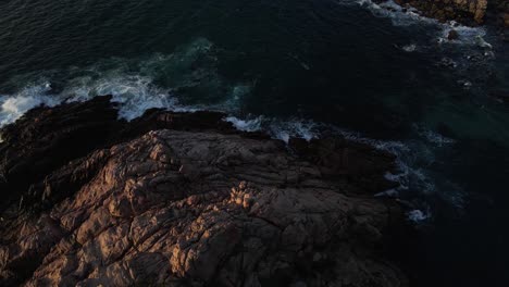 aerial flight along the coast of western australia with waves crashing on the shore during sunset