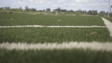 green artificial turf soccer field waiting for upcoming match, white lines marking playing area under bright sunlight and open sky