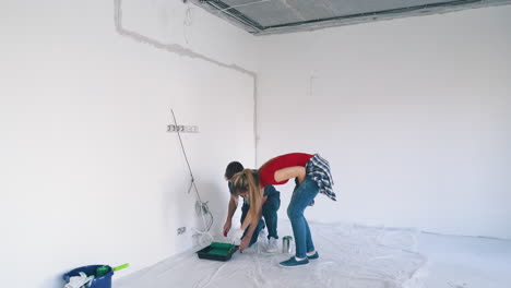 happy man with pretty wife begins painting white room wall