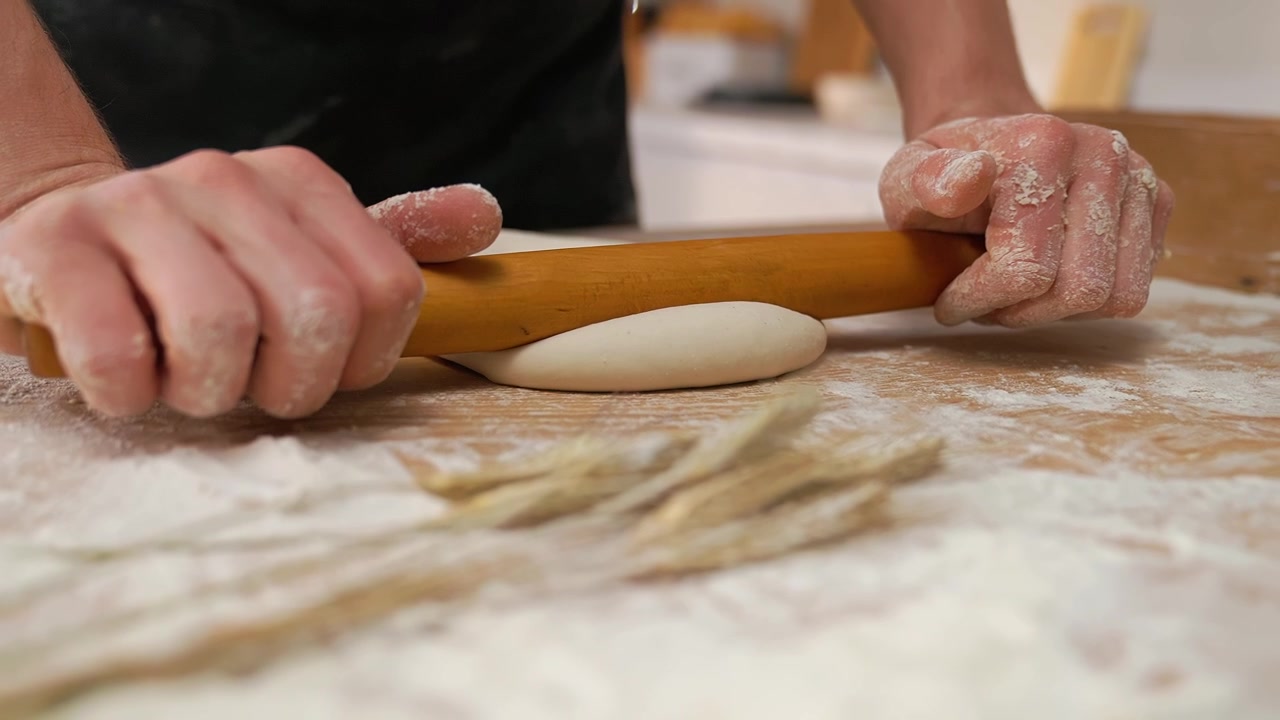 Mani che stendono l'impasto con un mattarello su un tavolo di legno infarinato
