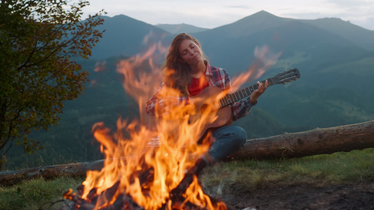 mujer sonriente tocando la guitarra en las montañas. campista feliz relajándose en el bosque de green hill.