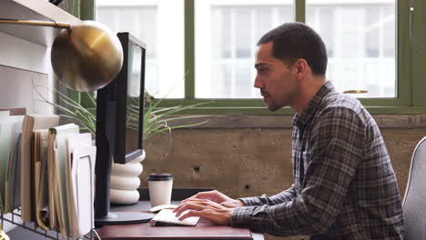 Junger-Hispanischer-Mann-Benutzt-Computer-In-Einem-Büro,-Seitenansicht