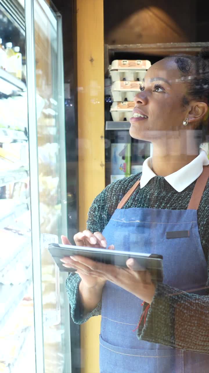 A woman in an apron checks stock in a refrigerator