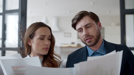 Closeup-focused-couple-reading-documents-at-home.-Partners-discuss-graphics.