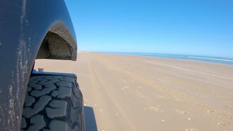 Right-front-tire-of-vehicle-and-the-surf-while-driving-on-a-beach-on-a-sunny-day-on-South-Padre-Island-Texas--Point-of-view,-POV