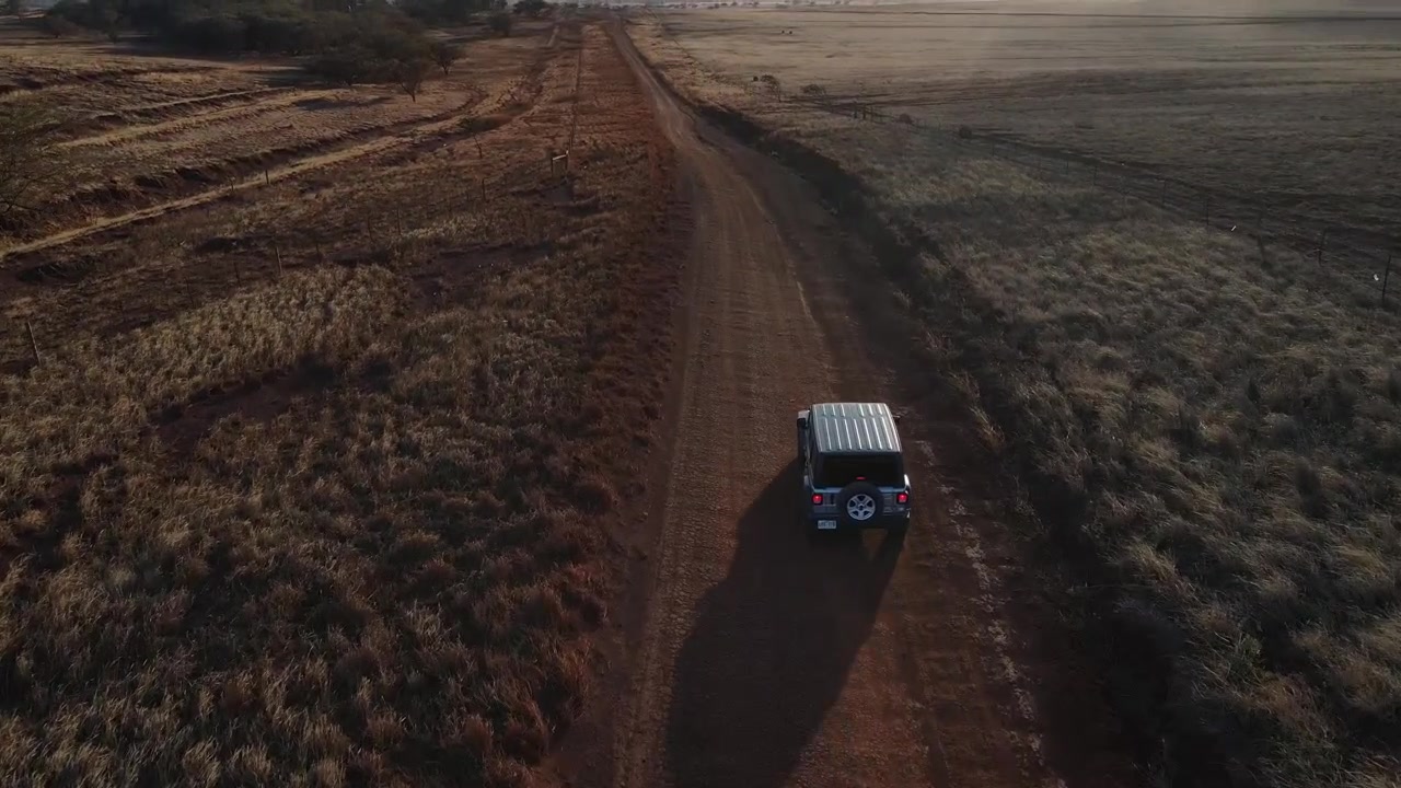 Aerea - Sorvolo di un SUV che guida su una strada sterrata in una mattinata di sole. Ripresa in tracking posteriore.