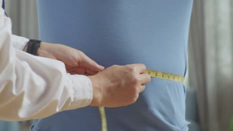 한 남성 환자의 허리를 측정하는 테이프를 사용하여 남성 의사 손의 근접