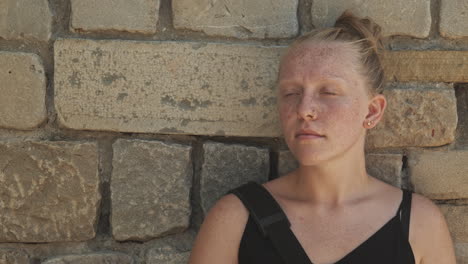 una mujer joven se sienta contra una pared de piedra en pensamiento tranquilo y reflexión