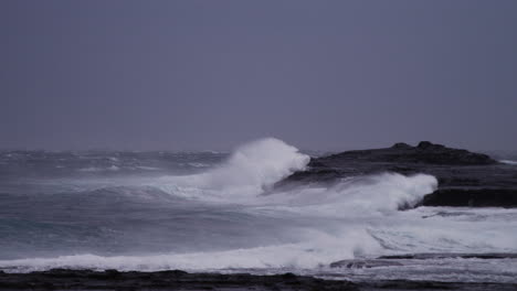 Stürmisch-Aussehender-Ozean,-Während-Ein-Extrem-Starker-Offshore-Wind-Die-Lippe-Der-Wellen-Anhebt,-Die-In-Zeitlupe-An-Den-Felsen-Brechen