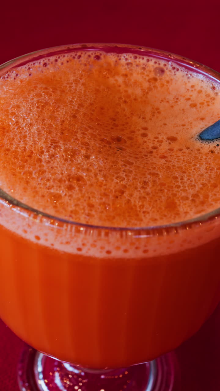 Primo piano di un succo di carota e arancia in un bicchiere con una cannuccia nera su una tovaglia rossa. Verticale