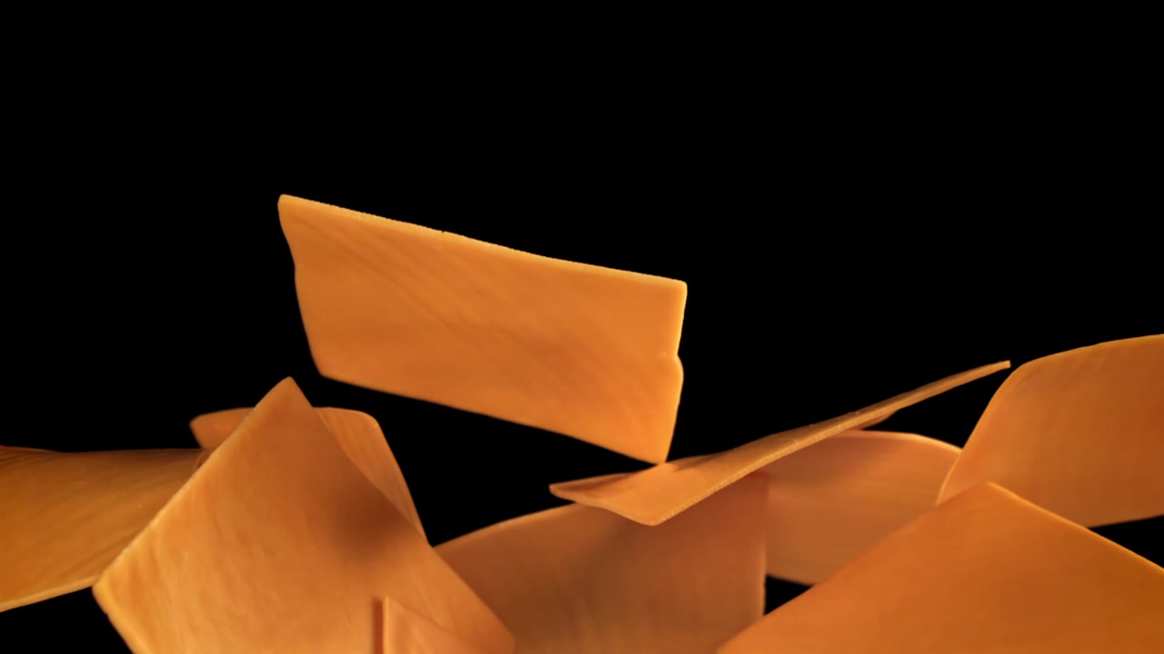 Movimento rallentato di fette di formaggio che cadono su sfondo nero