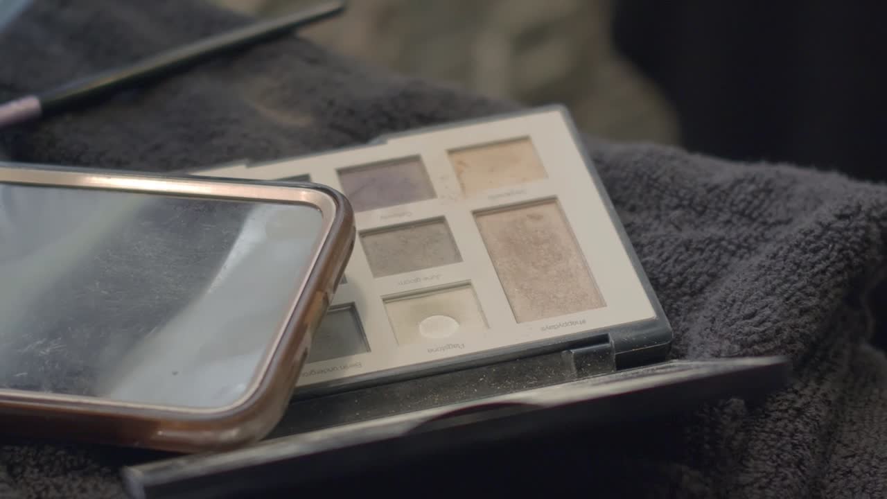 Close-up of an eye shadow palette with a phone and a towel, make-up