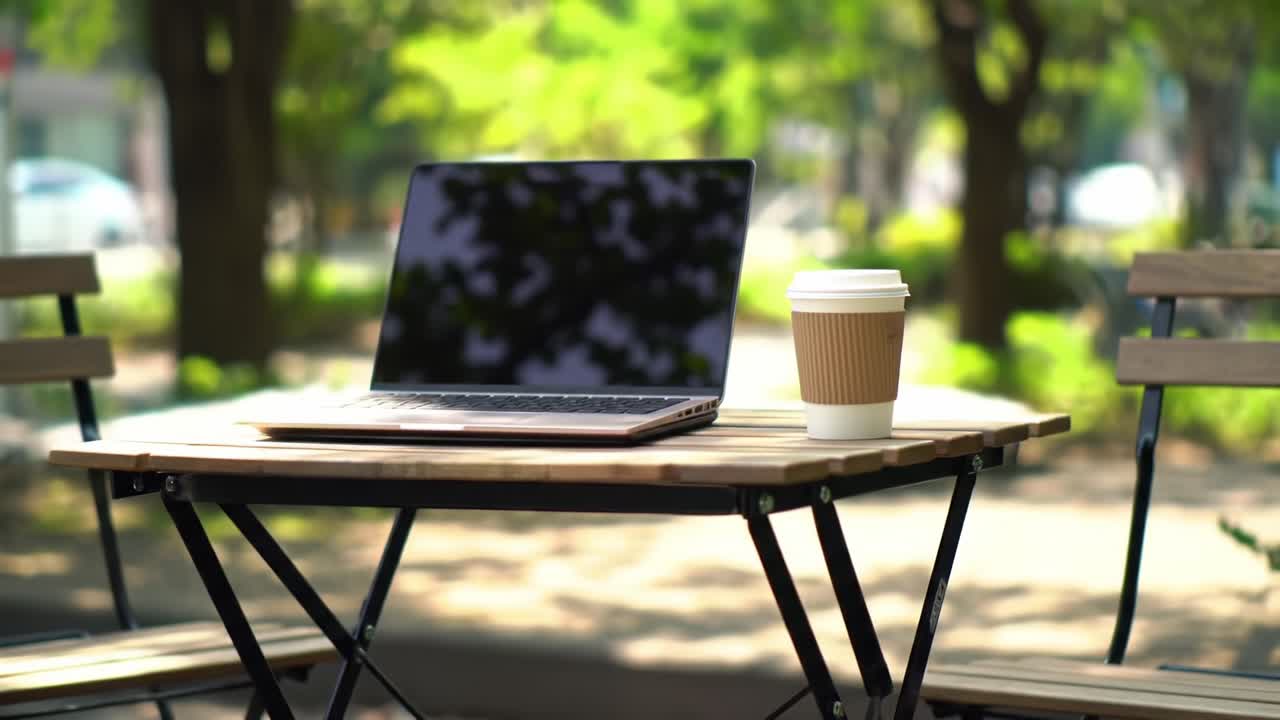 Un espacio de trabajo tranquilo al aire libre con un elegante portátil y una humeante taza de café sobre una mesa de madera, rodeado de exuberante vegetación y una suave luz solar, perfecto para la productividad