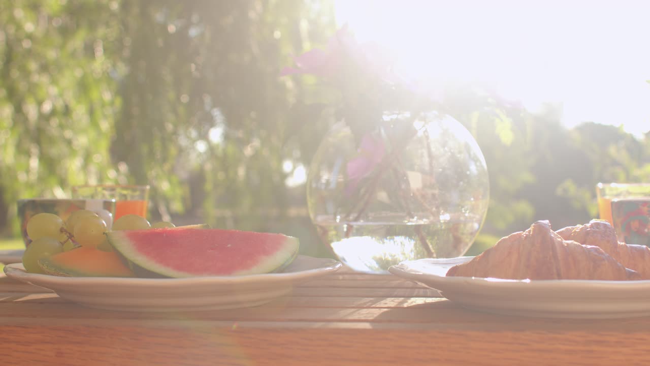 Fresh breakfast on the table. Fruit, glass, flowers in a vase. Sunlight.