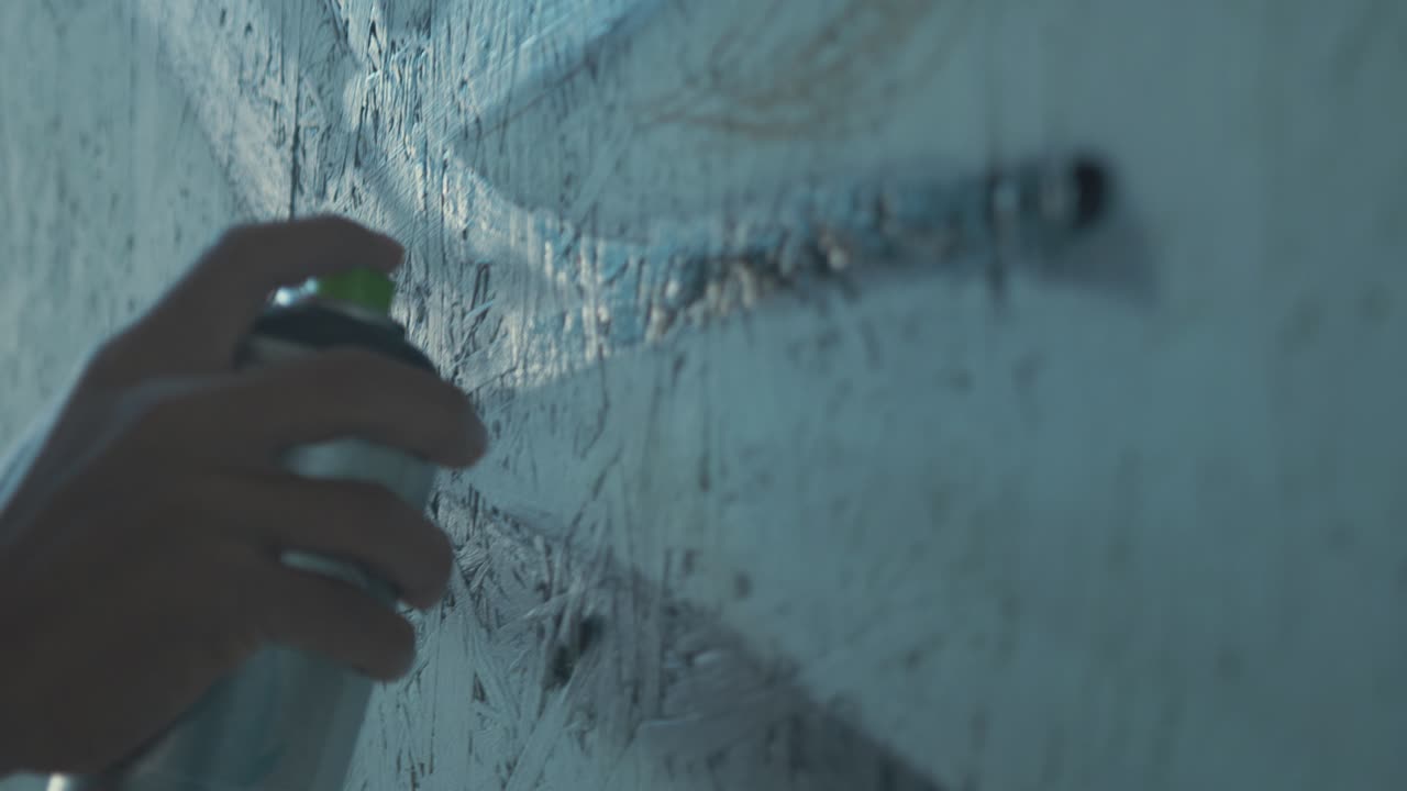 스프레이 페인트를 위해 가까이 가면 그래피티 아티스트가 벽에 검은 윤을 스프레이합니다.