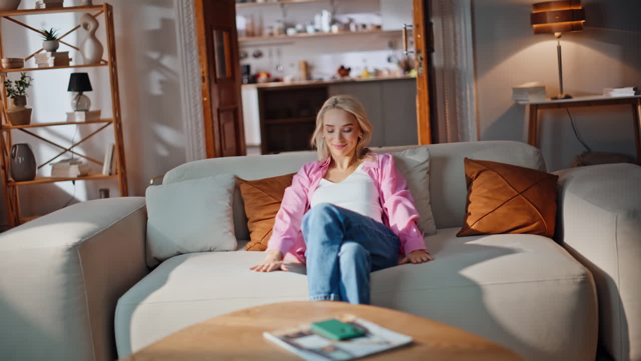 Content woman falling couch touching pillows at living room. Happy lady sitting