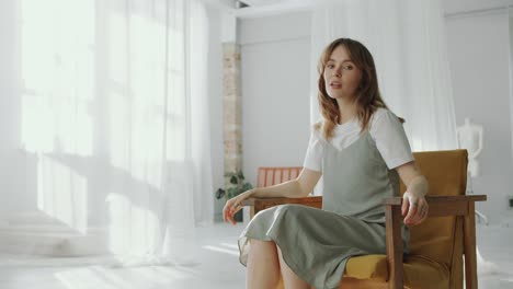 pretty woman posing on camera in armchair in studio with minimalist interior