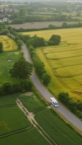 vertical drone shot tracking a camper driving in middle of blooming canola fields