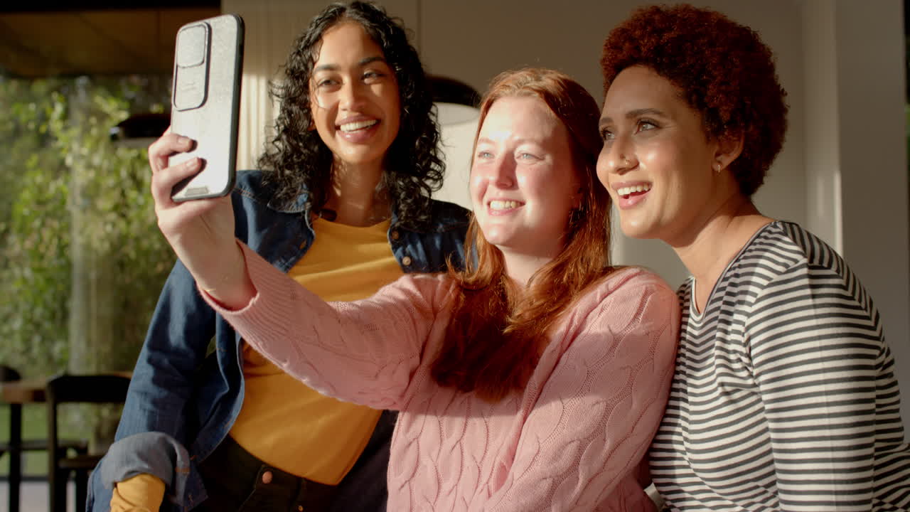 Taking selfie, diverse female friends smiling and enjoying time together indoors