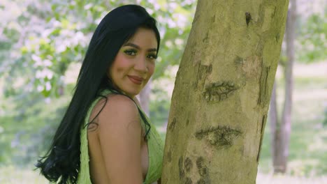 a young woman in a green dress hugs a tree trunk in a tropical park on the caribbean island of trinidad