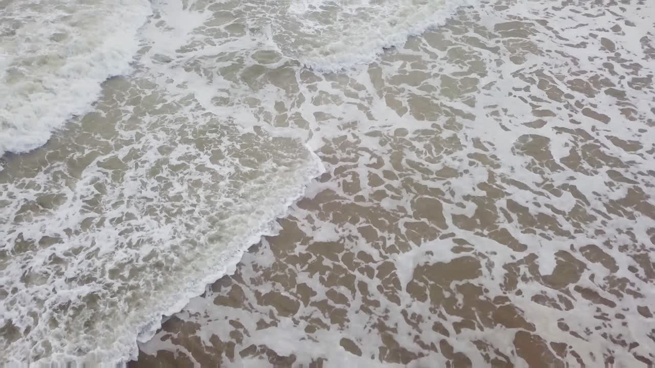 Waves gently crashing on a sandy shore in Scotland with foam spreading across the beach