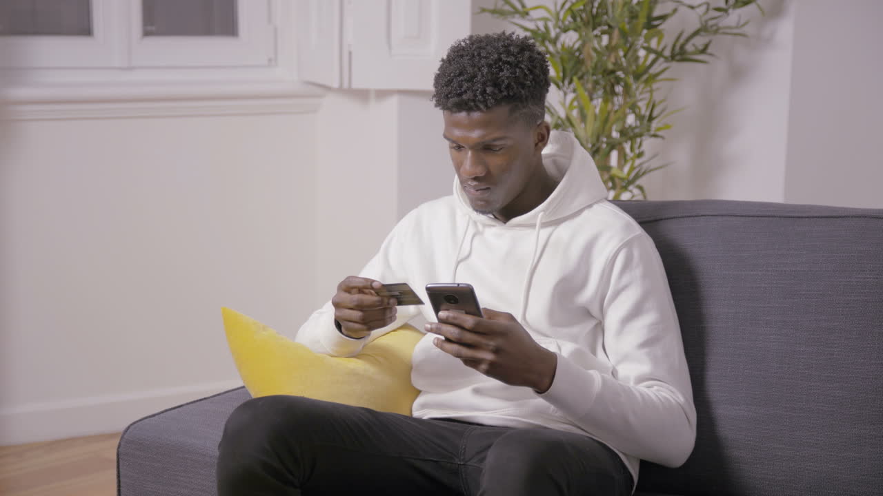 Serious young man typing card number for payment via smartphone