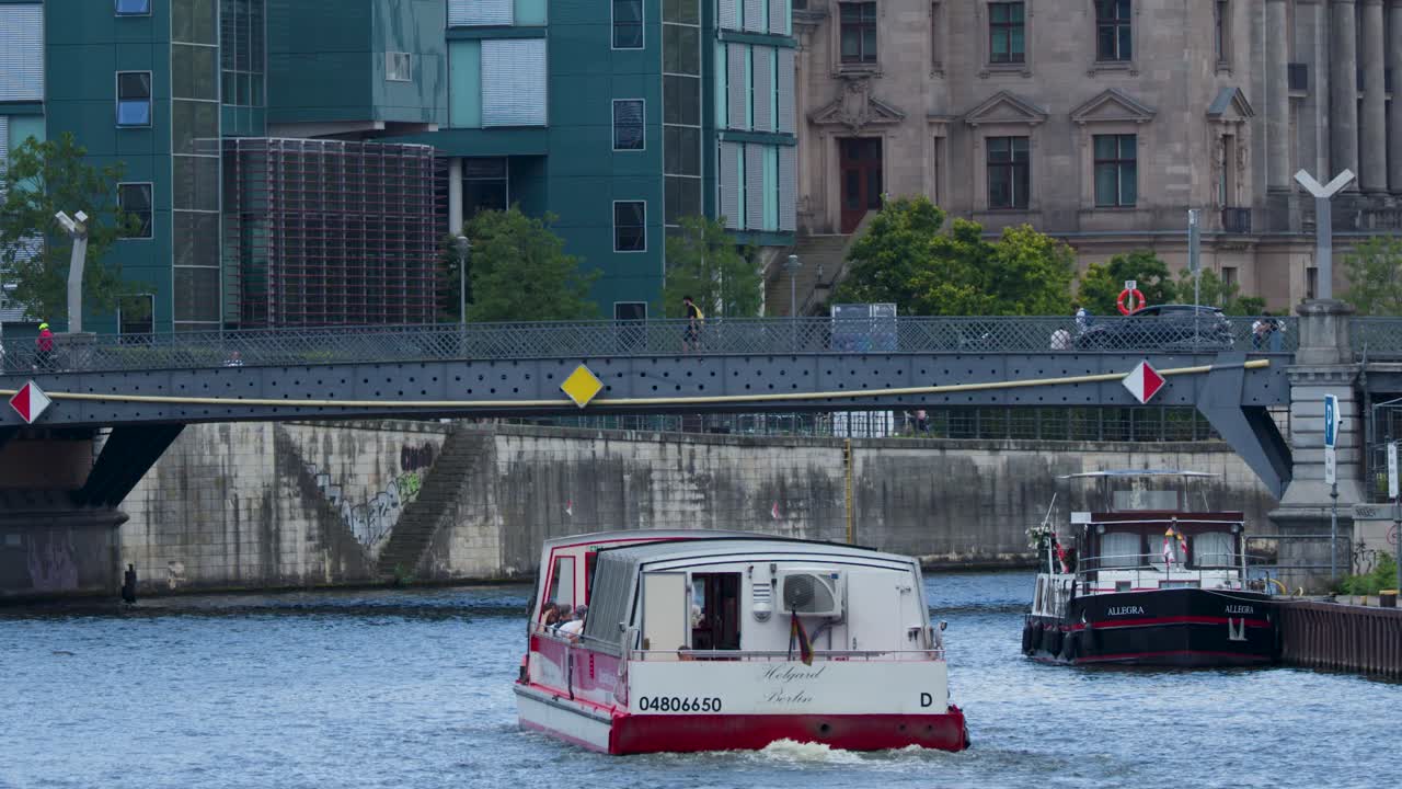Two tour boats pass under a city bridge on a Berlin river during cloudy daylight