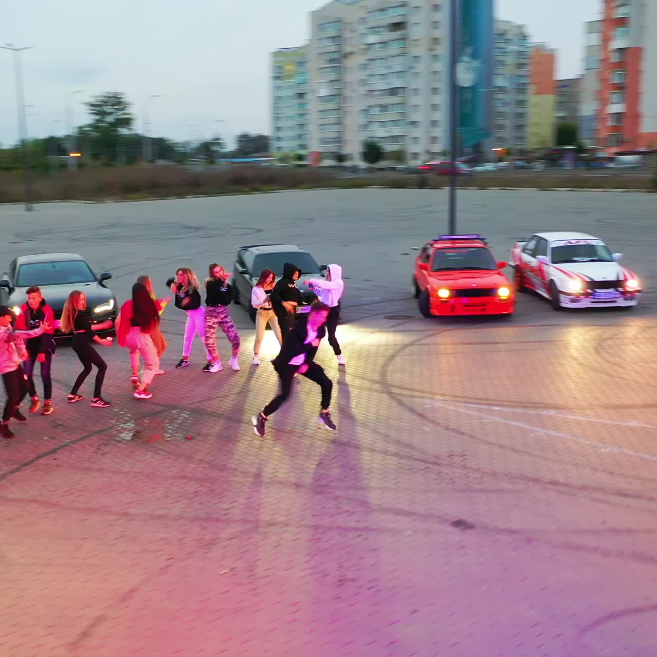 Happy young dancers in the middle of the square. Race cars are surrounding the teenage band. Top view