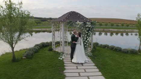 Recién-Casados,-Novio,-Novia-Abrazando,-Abrazos,-Besos,-Ceremonia-De-Matrimonio,-Arco-Con-Flores