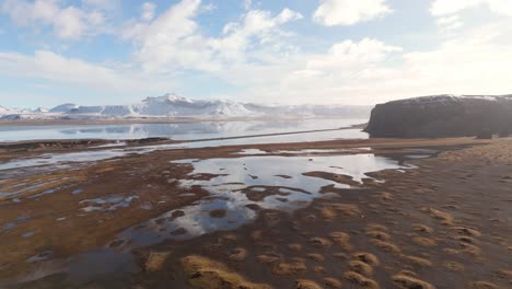 Snowy-mountains-in-Iceland-reflect-in-water-aerial,-sunny-day-travel-landscape