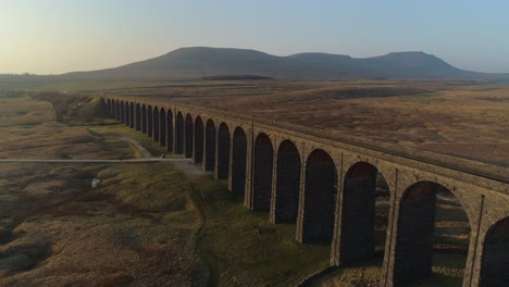 Niedrige-Luftdrohne-Schoss-Nahaufnahme-Zur-Ribblehead-Viadukt-Zugbrücke-Bei-Atemberaubendem-Sonnenaufgang-Im-Sommer-In-Yorkshire-Dales-England-Großbritannien-Mit-3-Gipfeln-Ingleborough-Berg-Im-Hintergrund