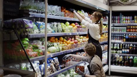 hombre y mujer trabajadores en delantal negro y guantes almacenando las frutas en el supermercado. joven empleado en el trabajo. lado