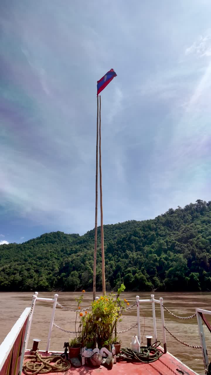 Bandiera del Laos che sventola su una barca che naviga sul fiume Mekong. Video verticale