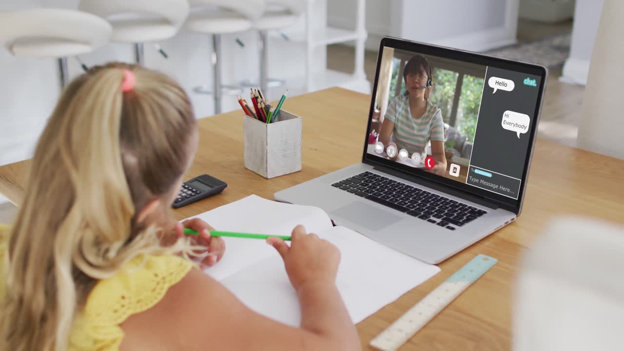 Schoolgirl using laptop for online lesson at home, with female teacher and webchat on screen