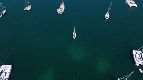 aerial high angle pan across anchored yachts and sailboats in calm, clear ocean waters, creating a serene scene
