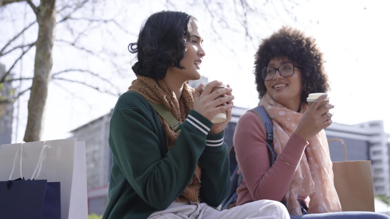 Diverse female friends tapping coffee cups to chat, sipping and pointing skyward on park bench