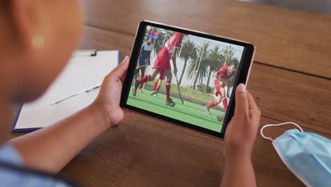 composite of woman sitting at table with face mask, watching hockey match on tablet