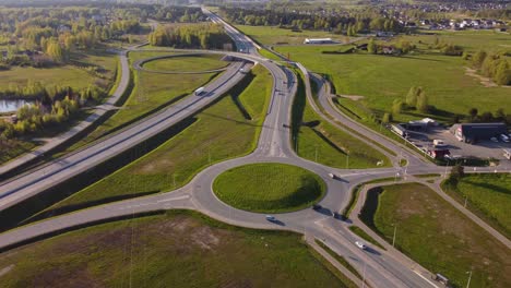 sweeping aerial of springtime traffic roundabout and nearby residential structures, drone angled approach