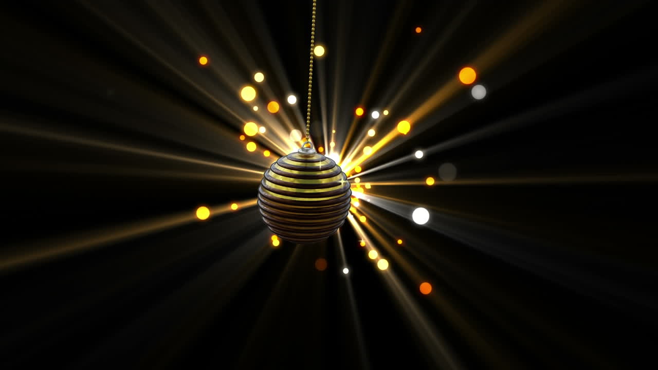 Swinging black and gold christmas bauble over starburst with yellow and orange light spots on black